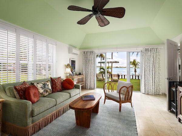 The image shows a living room with green walls and ceiling, tropical-themed furniture, and a view of a patio leading to a lawn with palm trees.