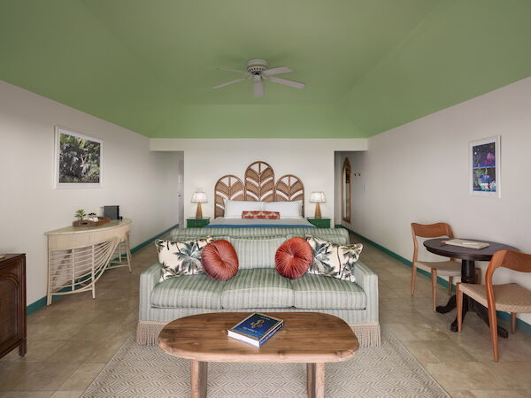 A cozy living room with a sofa, coffee table, bed, two lamps, a small desk, and chairs, decorated with vibrant cushions and wall art, ends the sentence.