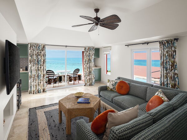 A spacious living room with wicker furniture, ocean-themed decor, and large windows revealing a stunning ocean view. Ends with a complete sentence.
