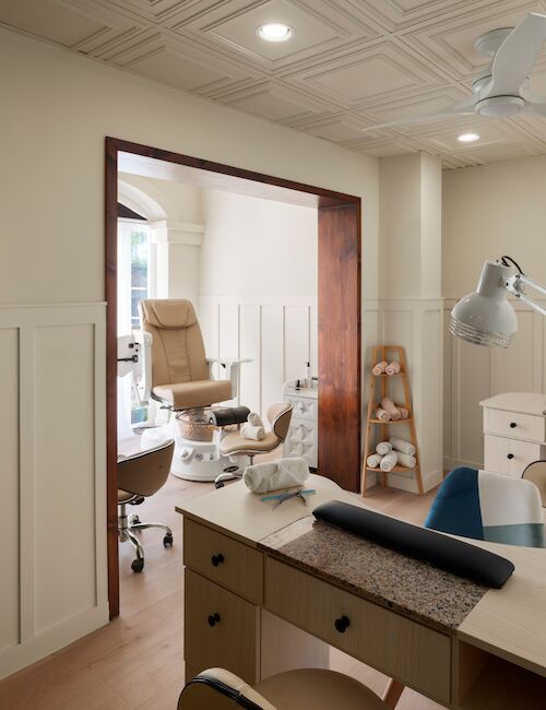 This image shows an interior of a nail salon with manicure stations, chairs, and lamps, offering a cozy and organized atmosphere.
