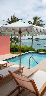 A poolside view with lounge chairs, an umbrella, and a scenic ocean backdrop with boats and palm trees.