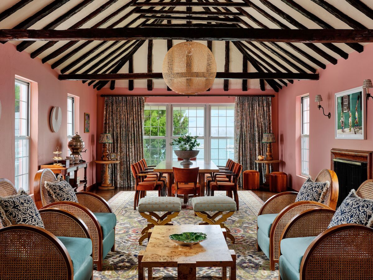 The image shows a cozy living room with pink walls, wooden beams, and stylish furniture, creating a warm and inviting atmosphere.