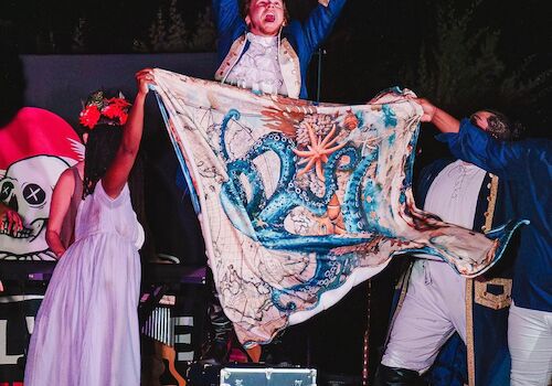 A performance with people on stage; one holds a colorful cloth featuring an octopus design, engaging the audience.