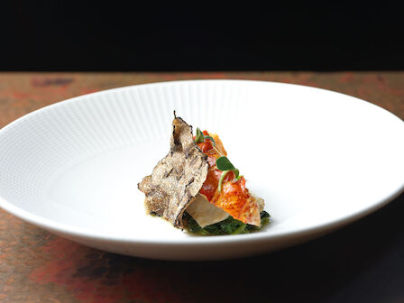 A gourmet dish on a white plate, featuring a delicate presentation with truffle slices and a garnish, set against a dark background.