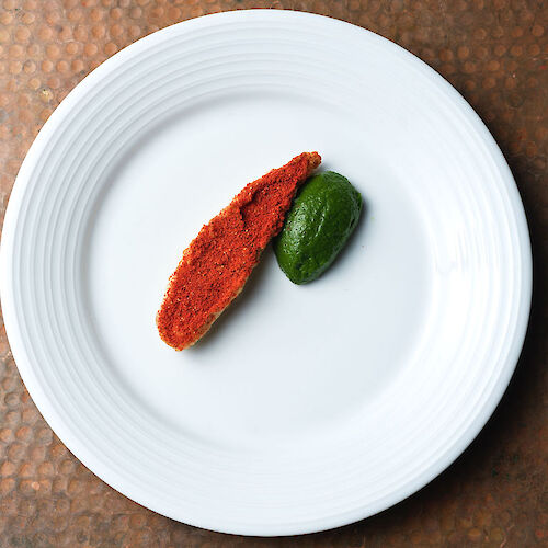 A white plate with a piece of red meat and a small green vegetable placed on it, on a textured brown surface.