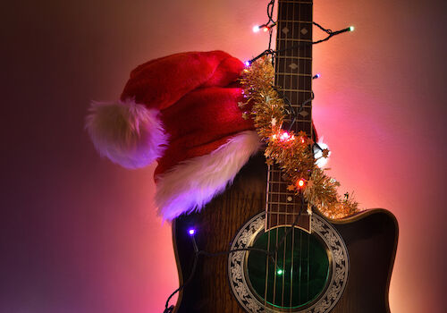 A guitar decorated for Christmas with a Santa hat and tinsel lights, glowing softly against a warm, festive backdrop.